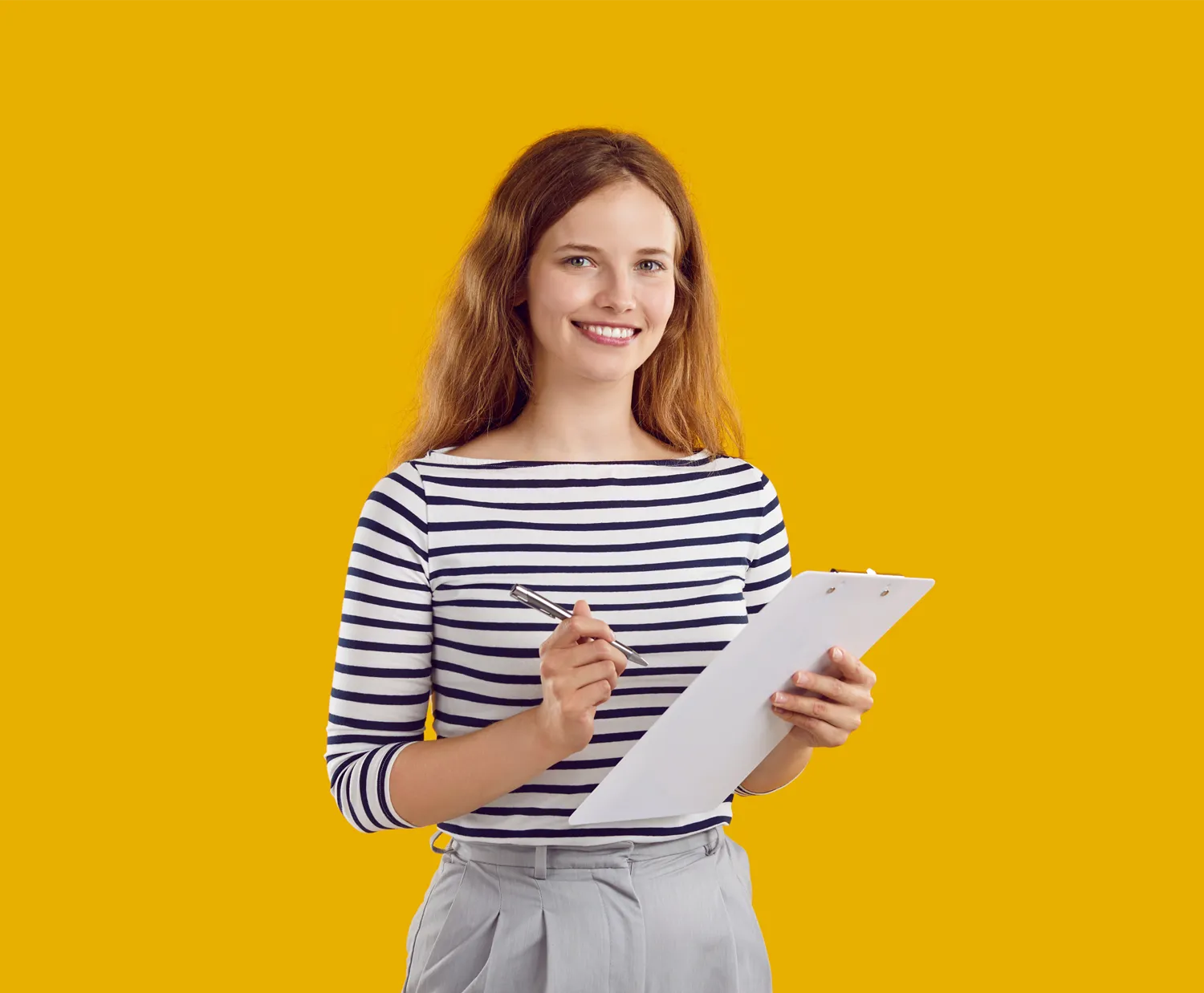 a lady holding writing instruments a notepad and a pen, looking at the camera smiling