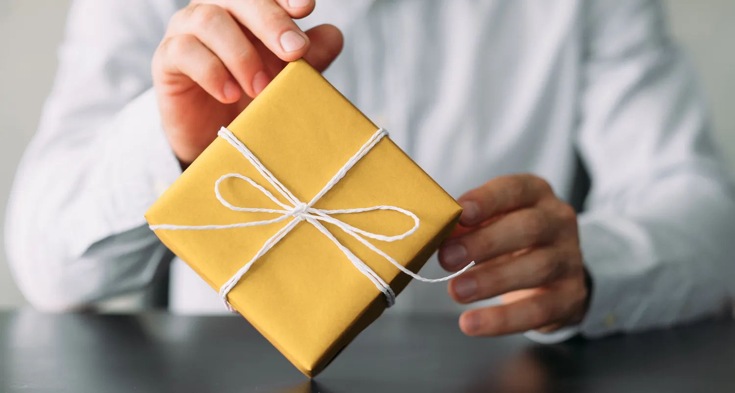 A man presenting a yellow gift box tied with a white ribbon for corporate gifting.