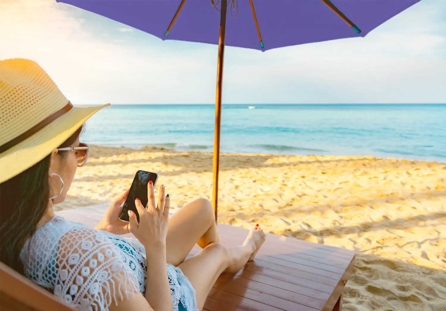 women sitting under a branded beach umbrella, looking at her phone