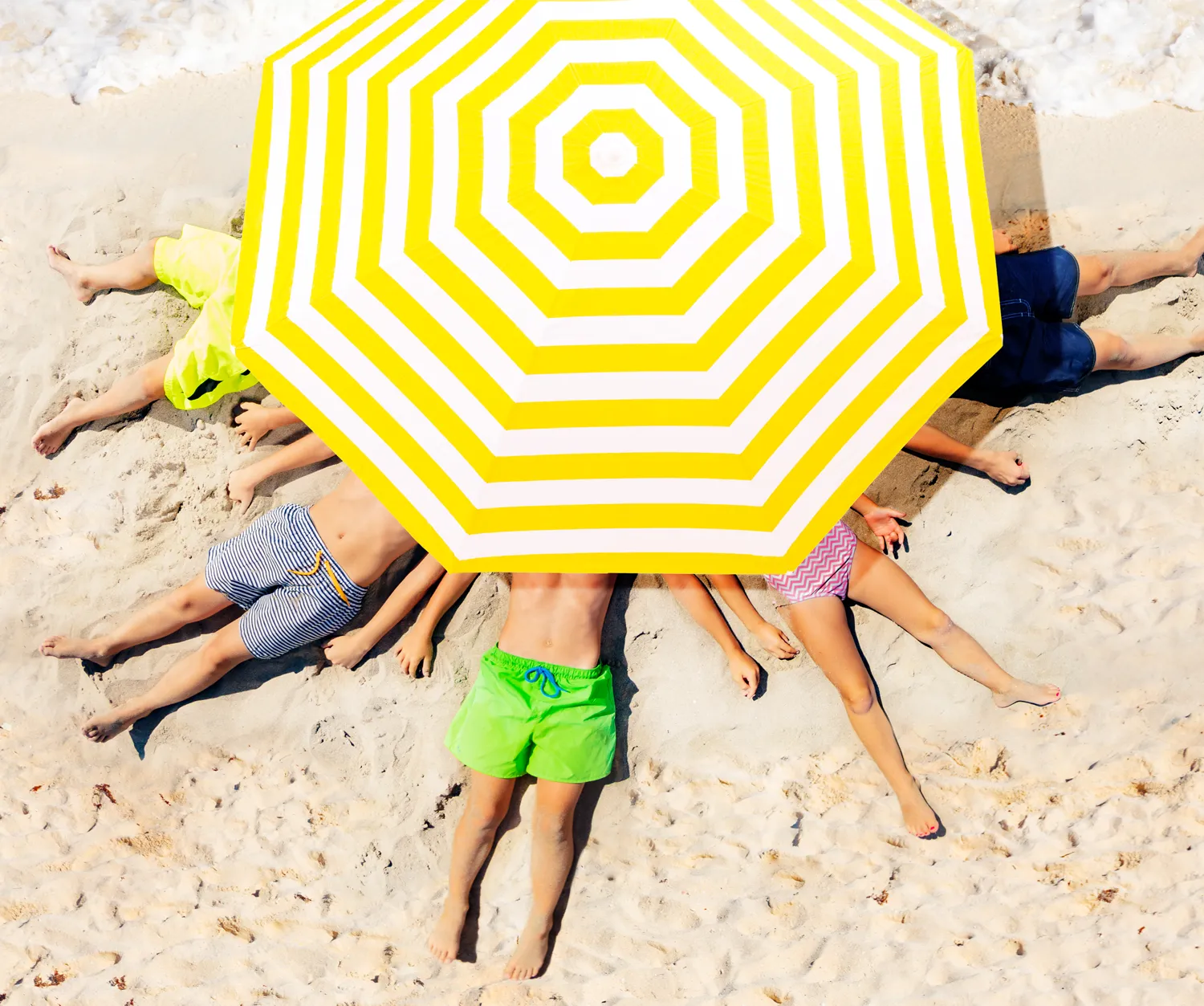 a group of people lying down underneath a branded beach umbrella
